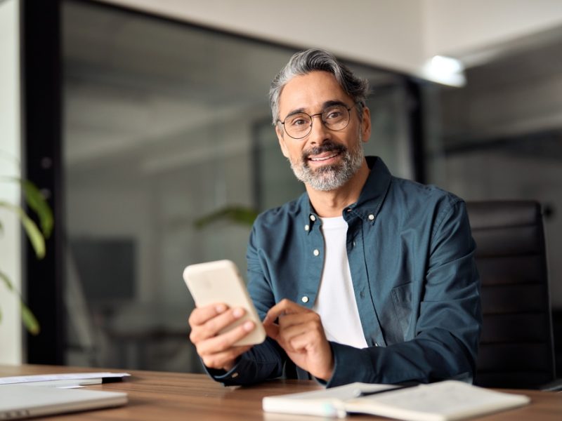 Middle,Aged,Businessman,Looking,At,Camera,Working,Holding,Smartphone.,Mature